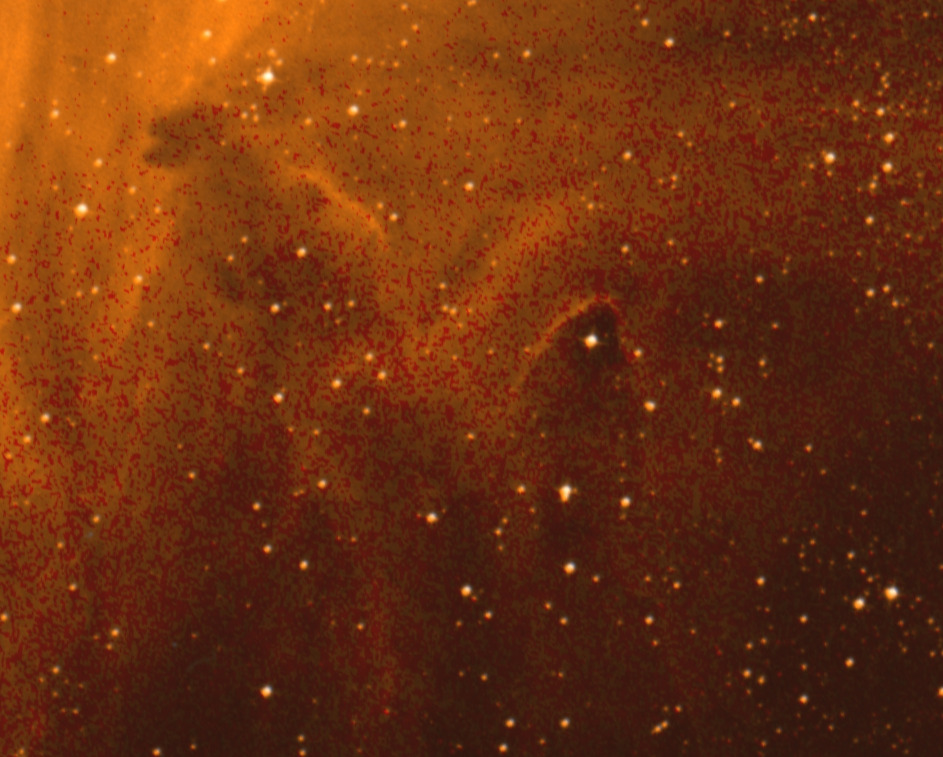 Mesma região da imagem anterior, no Digital Sky Survey. A imagem é toda alaranjada e as regiões mais escuras vistas na imagem anterior já não são tão nítidas. Em primeiro plano há diversas estrelas de cor branca espalhadas pelo campo de visão inteiro.