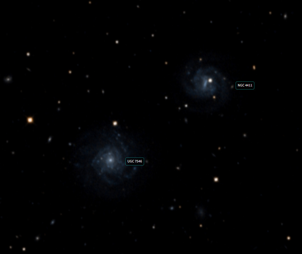 Mesmo campo da figura anterior, só que na imagem do Digital Sky Survey.
Imagem do céu profundo mostrando duas galáxias espirais com etiquetas de identificação. No canto inferior esquerdo, está a galáxia UGC 7546, com braços espirais sutis e estrutura azulada. Acima e à direita, encontra-se a galáxia NGC 4411a, também espiral, com brilho central mais intenso. Ambas estão cercadas por diversas estrelas pontuais e pequenas galáxias de fundo, em um campo escuro e repleto de objetos celestes distantes.